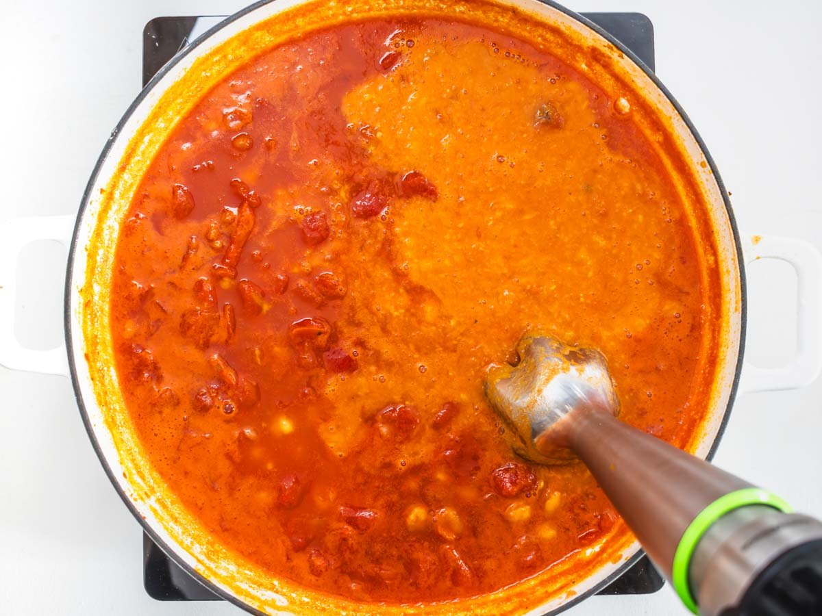 handblender in a skillet blending tomato sauce and chickpeas