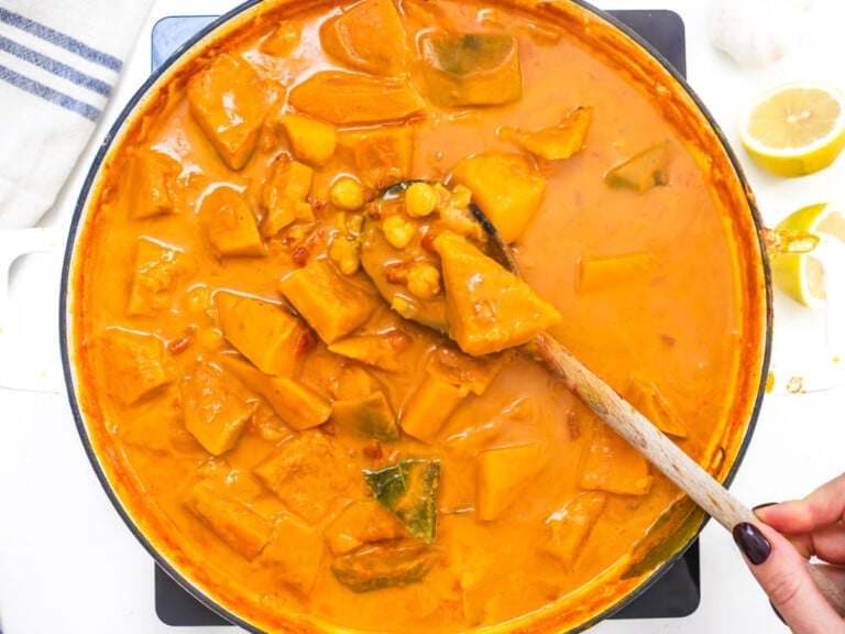 creamy curry sauce with pumpkin and chickpeas with hand holding a spoon