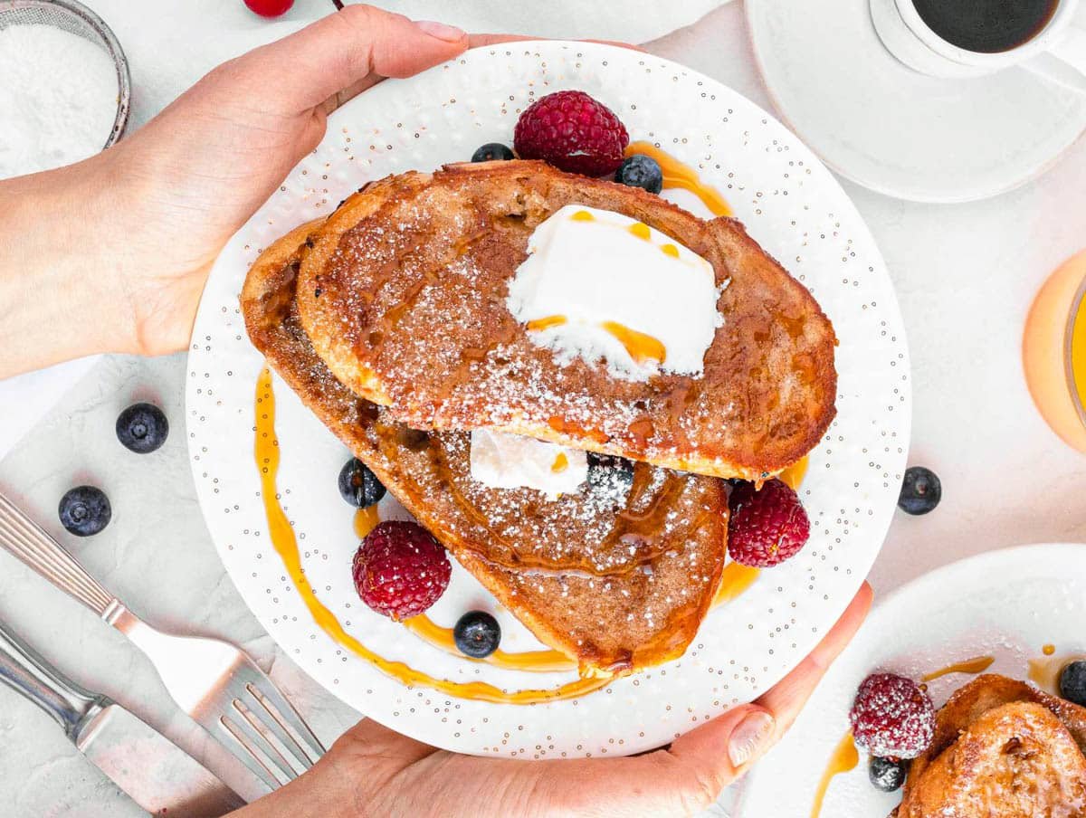 Vegan French toast on a white plate with hands