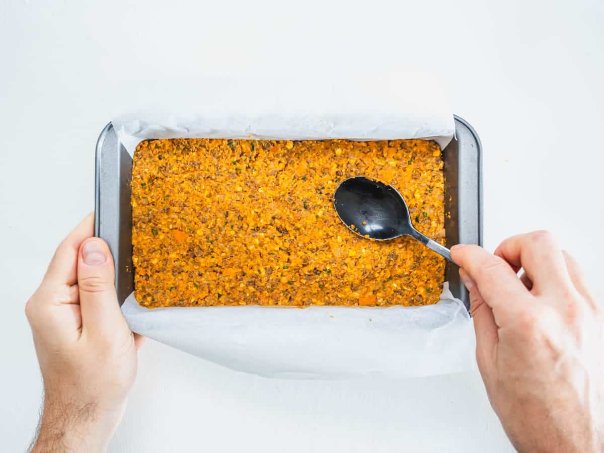 lentil loaf in a loaf pan with hands and spoon