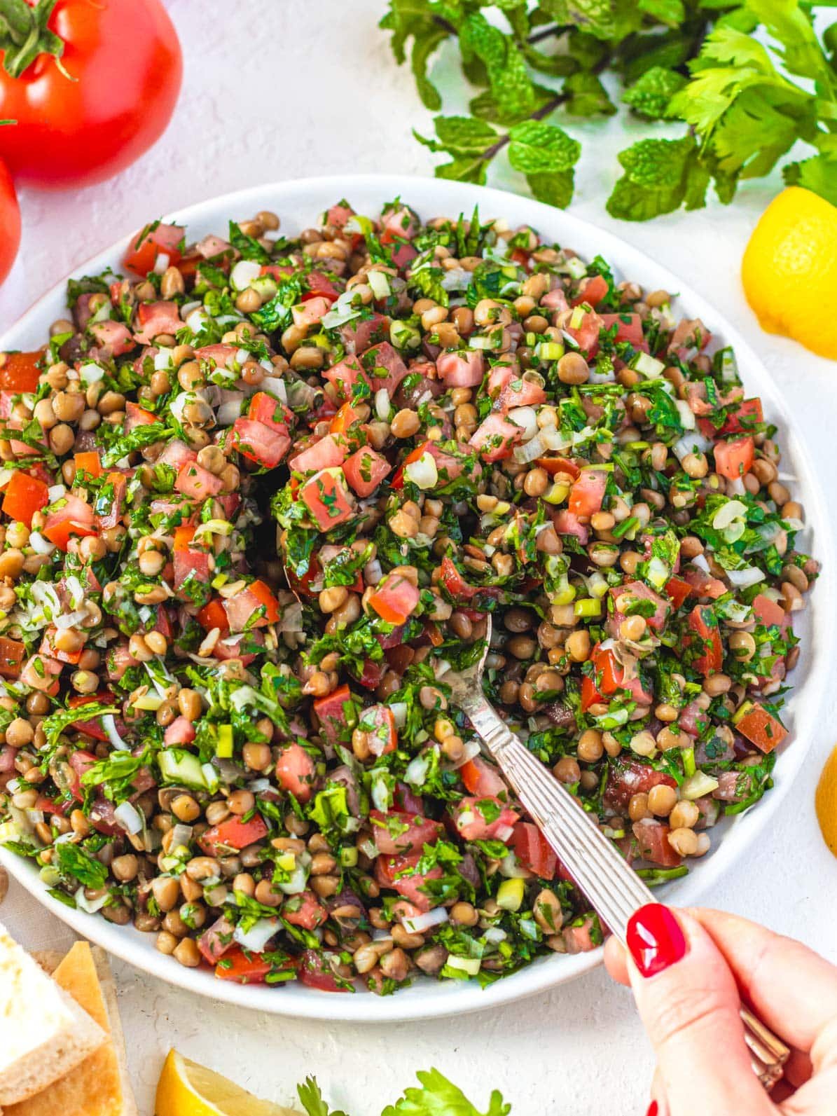 Lentil tabbouleh on a plate with a hand and red nail