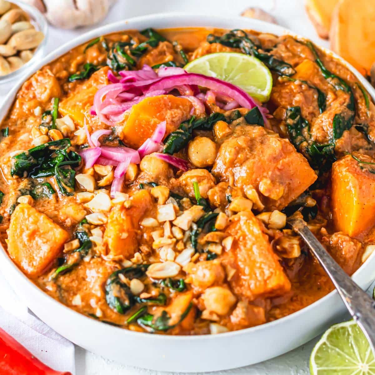 African peanut stew in a white bowl with pickled red onions and lime wedge