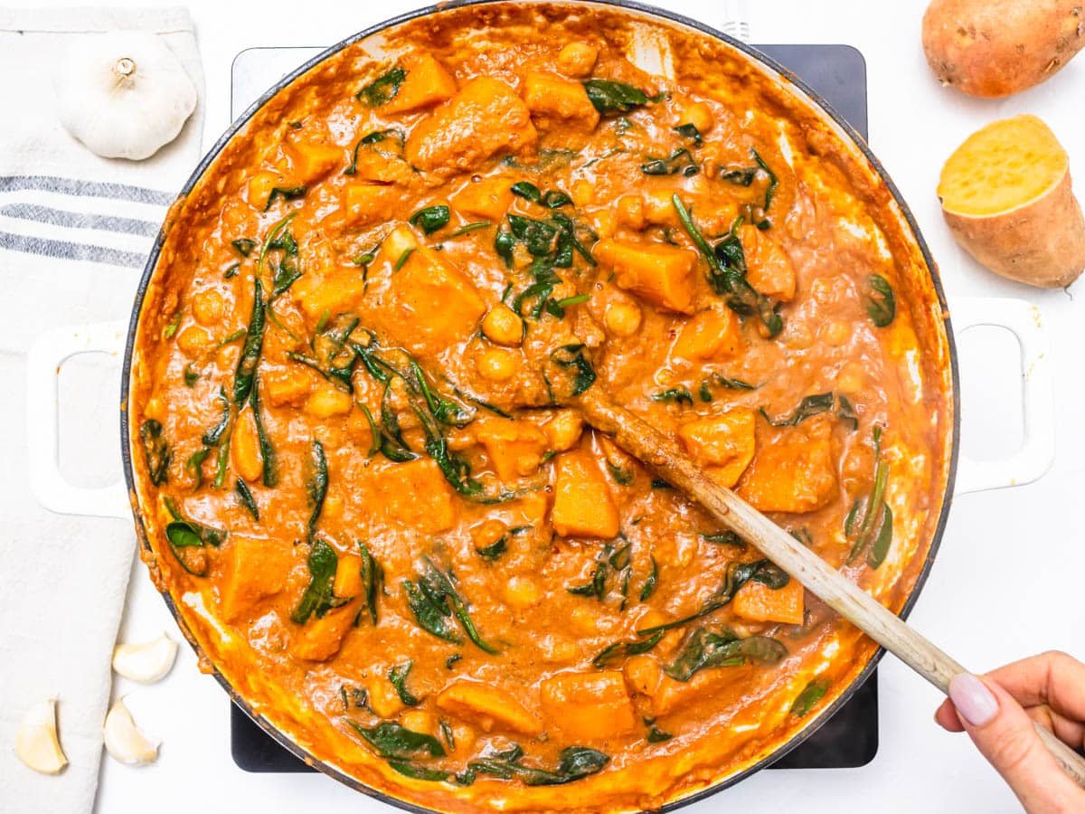 creamy stew with sweet potato and spinach in a skillet with a wooden spoon