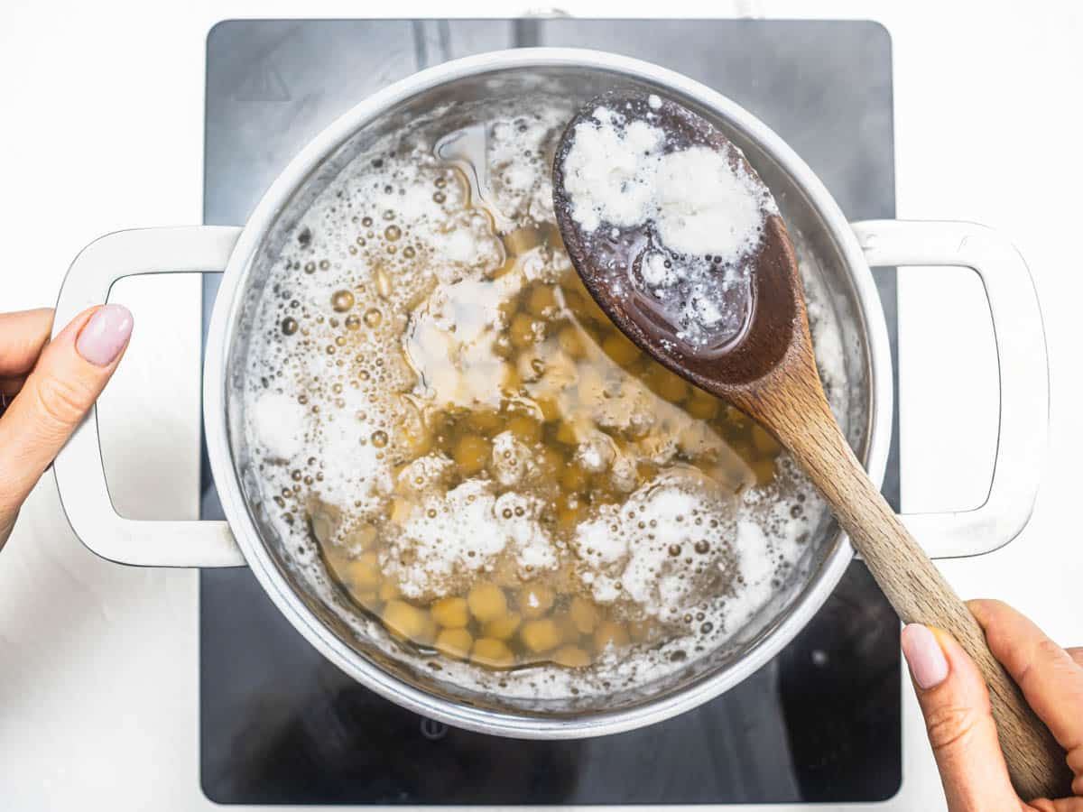 Chickpeas cooking on stovetop and removing foam with wooden spoon