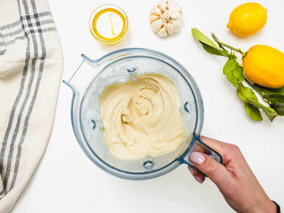 Hummus without tahini in a blender and a hand holding the handle