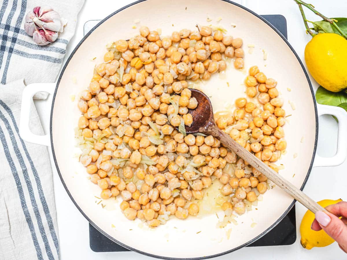 skillet with chickpeas and onion and hand holding a spoon