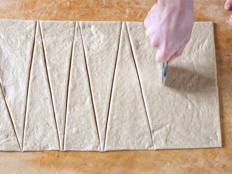hand cutting dough into triangles for croissants