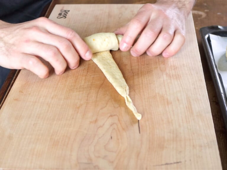 hands rolling dough into croissant shape