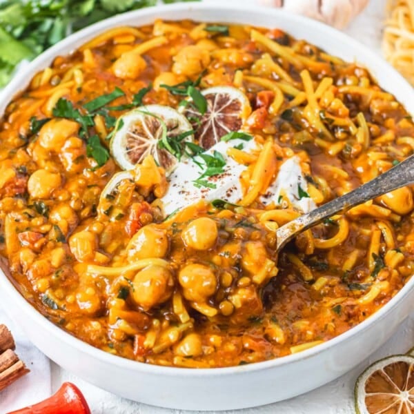 harira soup in a white bowl scooping chickpeas and pasta