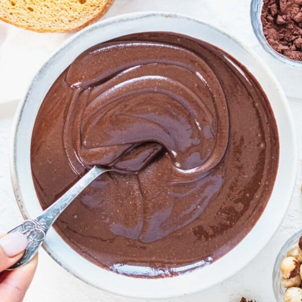 hazelnut spread in a bowl with a silver spoon and hand holding the spoon