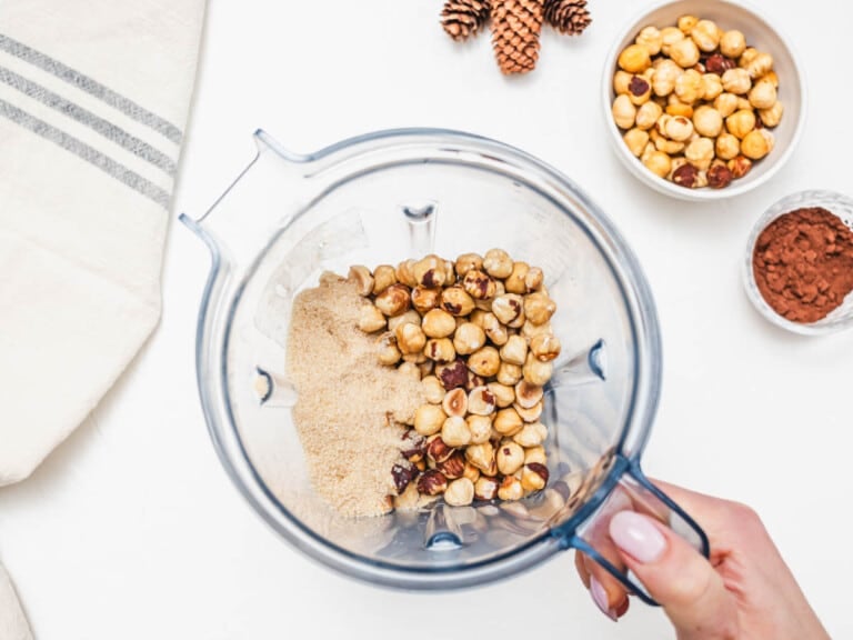 sugar and toasted hazelnuts in a high speed blender with hand holding the blender