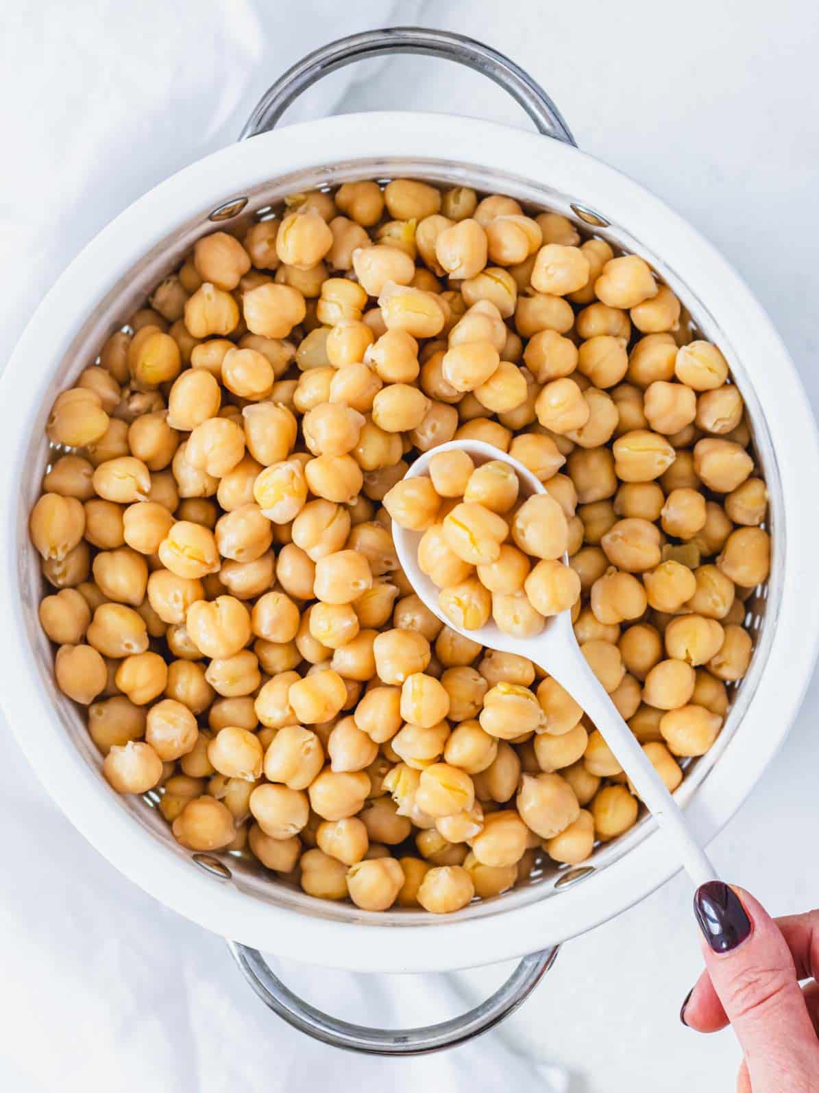 cooked tender chickpeas in a white sift with hand holding a white spoon