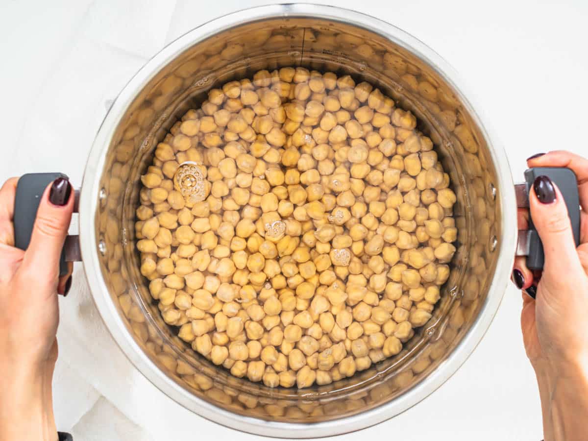 chickpeas after 12 hours of soaking in a big pot with hands holding the pot