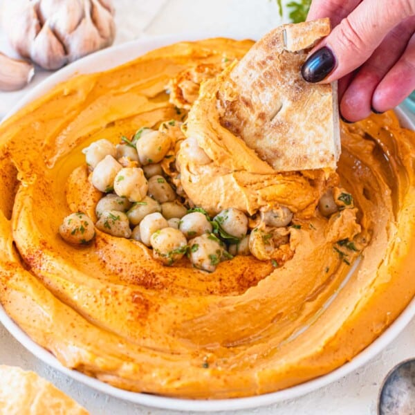 roasted red pepper hummus with chickpeas and hand holding a pita chip