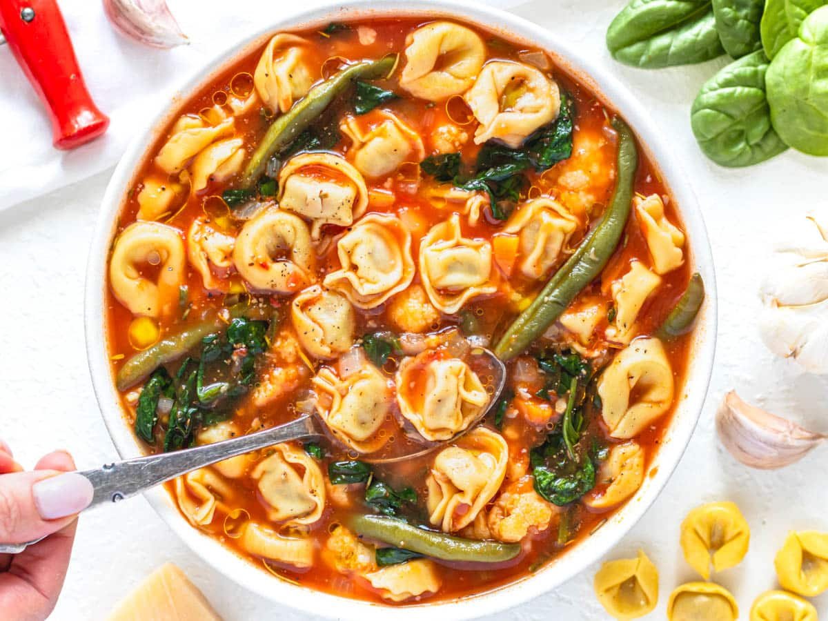 tortellini soup with spinach and hand holding a silver spoon