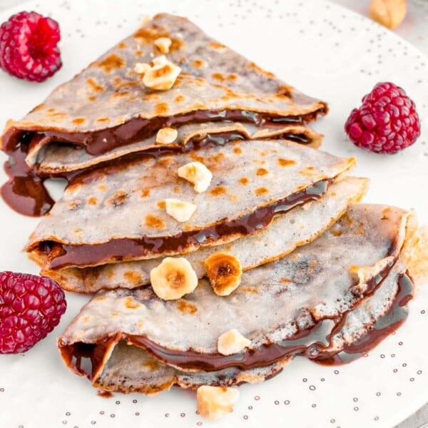 vegan crepes on a white plate with hazelnuts and berries