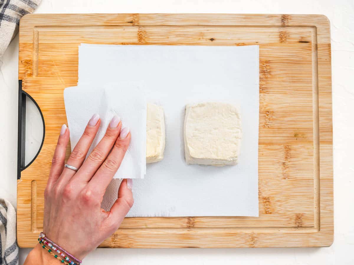 pressing tofu with a hand and kitchen towel