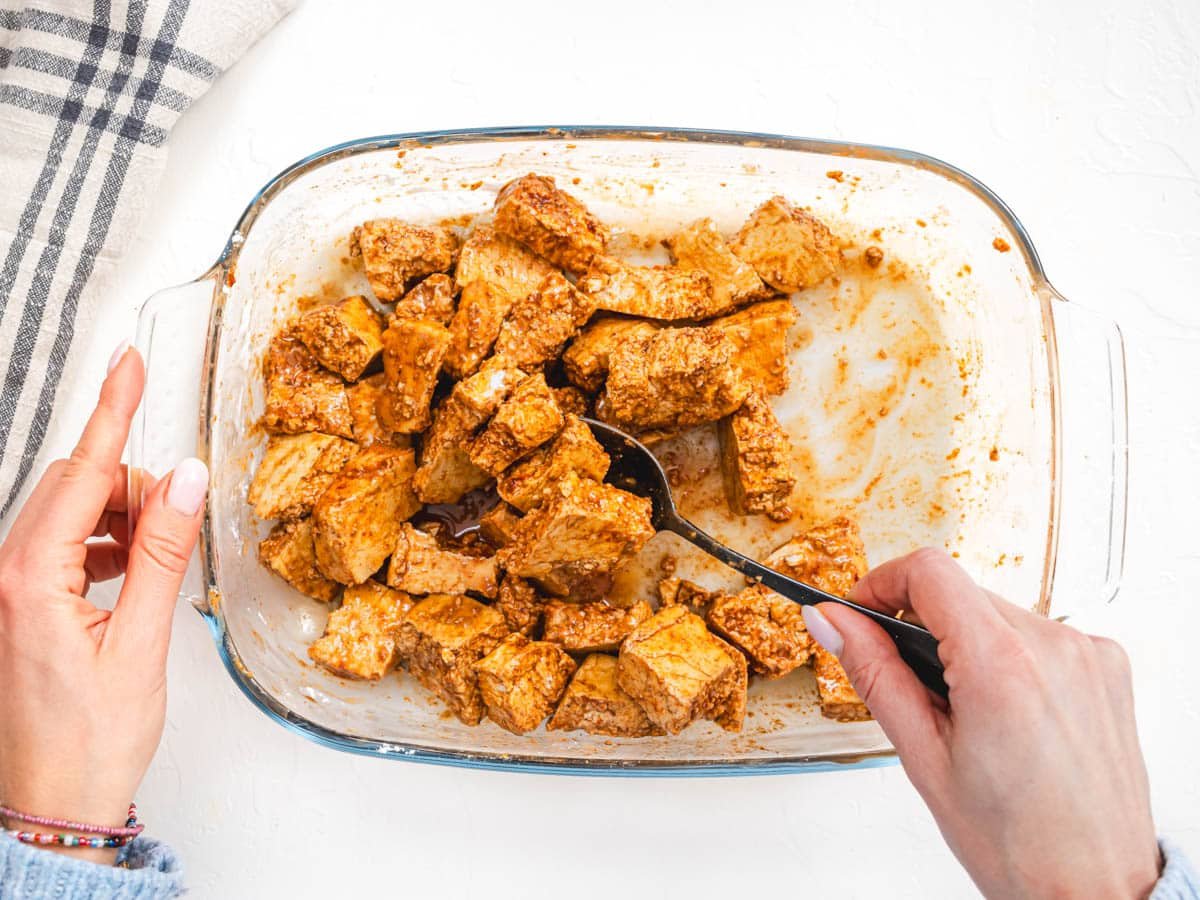 tofu pieces and hands mixing them in a marinade