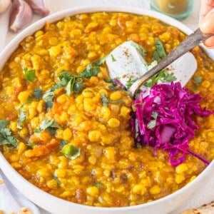 Chana Dal in a white bowl with pickled cabbage and hand holding a spoon