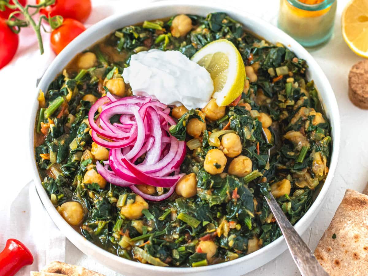 Chana Saag with lemon and pickled onions in a white bowl