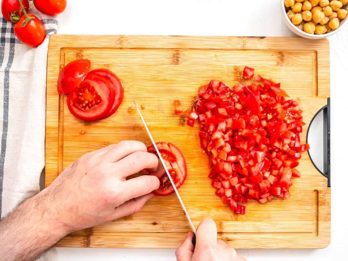 Hands chopping tomatoes on a cutting board