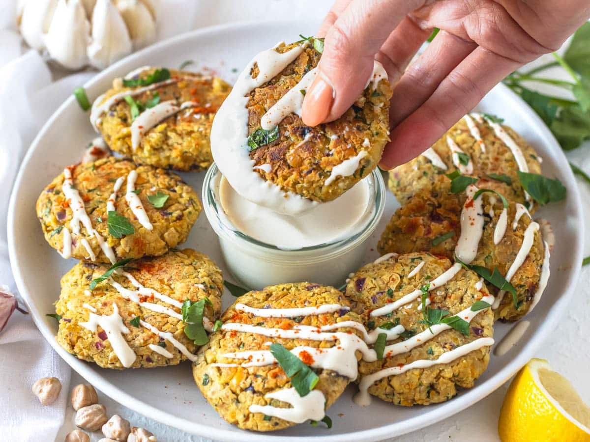 Chickpea fritters held by a hand and tahini dip in the middle