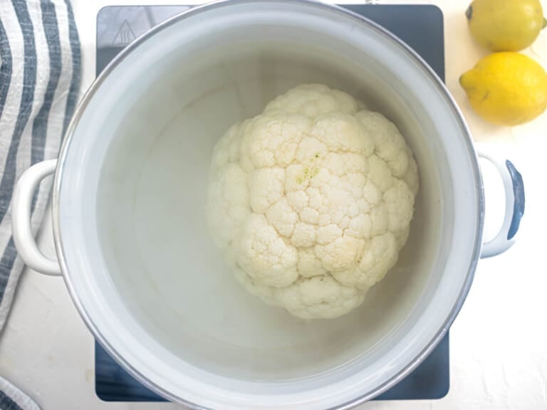 whole head of cauliflower boiling in a white pot