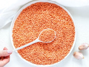 dried red lentils before cooking with a white spoon and a hand