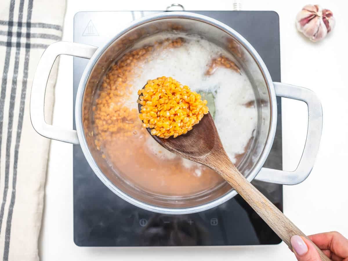 red lentils cooking in a casserole and a wooden spoon