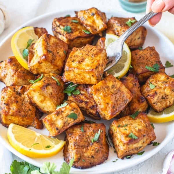 Marinated tofu with lemon slices and fresh parsley with hand holding a fork