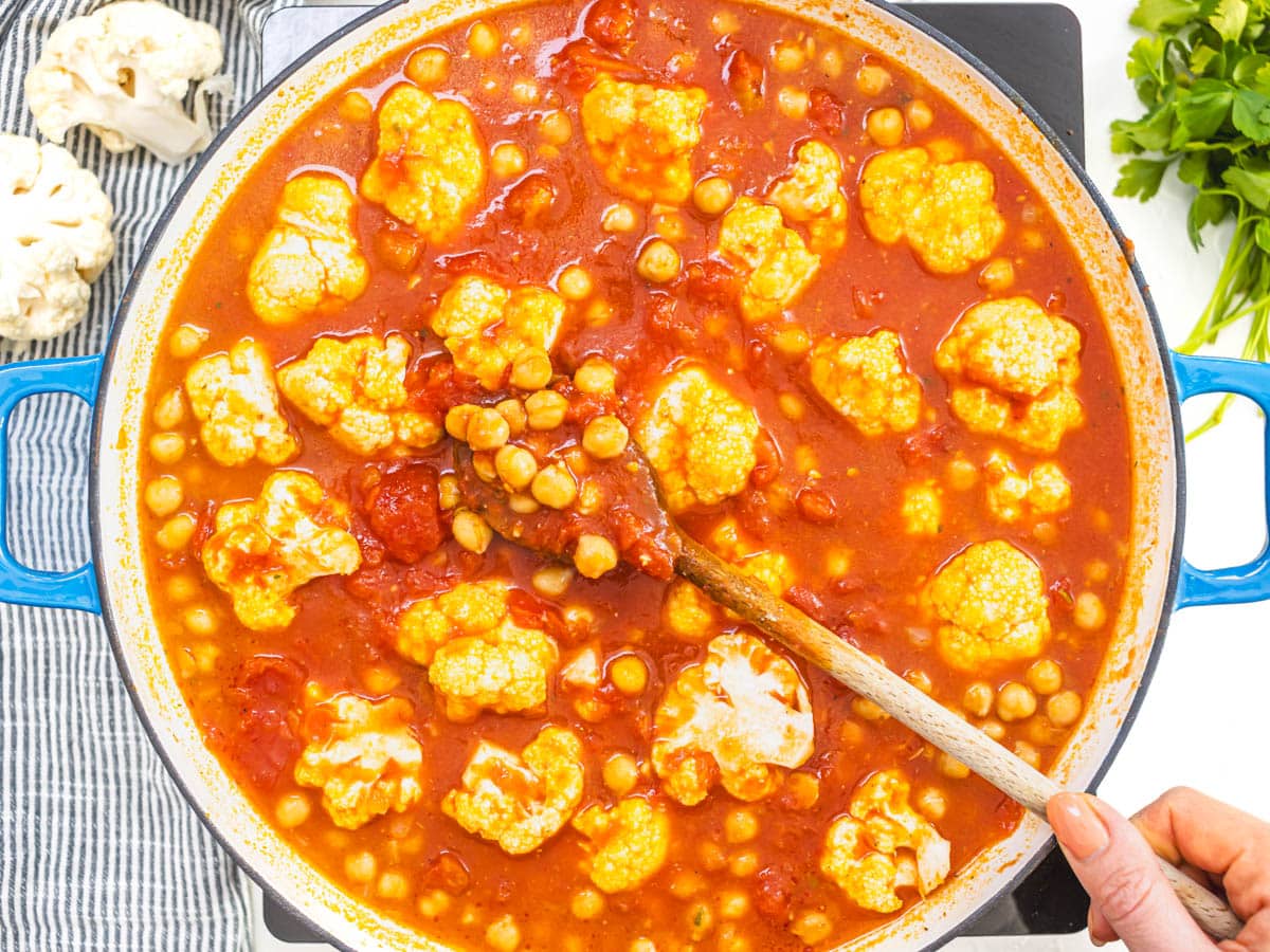 tomatoes, broth, cauliflower and chickpeas in a blue skillet