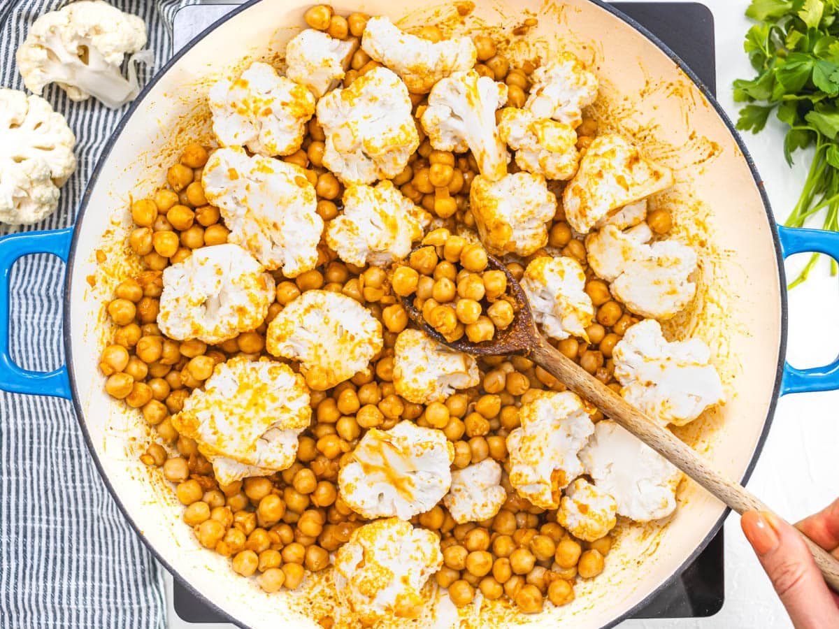 cauliflower florets, chickpeas, and a wooden spoon in a skillet
