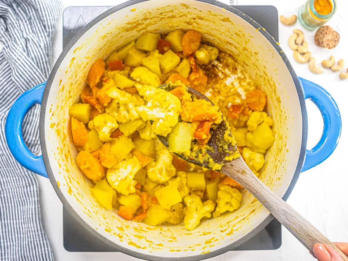 chopped vegetables with turmeric and spices in a blue pot and hand holding a spoon