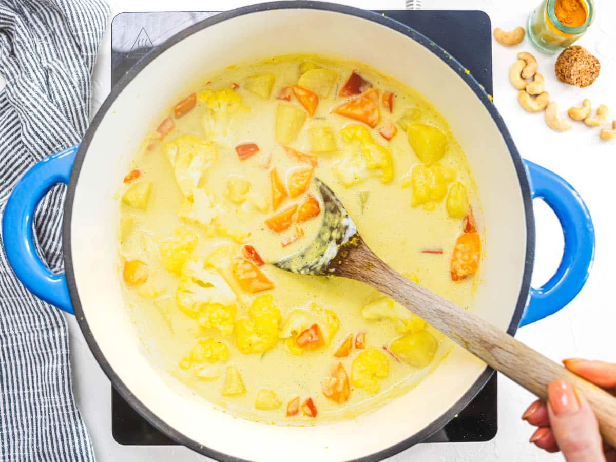 vegetables, coconut milk and a wooden spoon in a blue pot