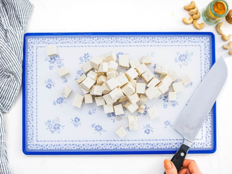 chopped tofu cubes on a cutting board with a knife