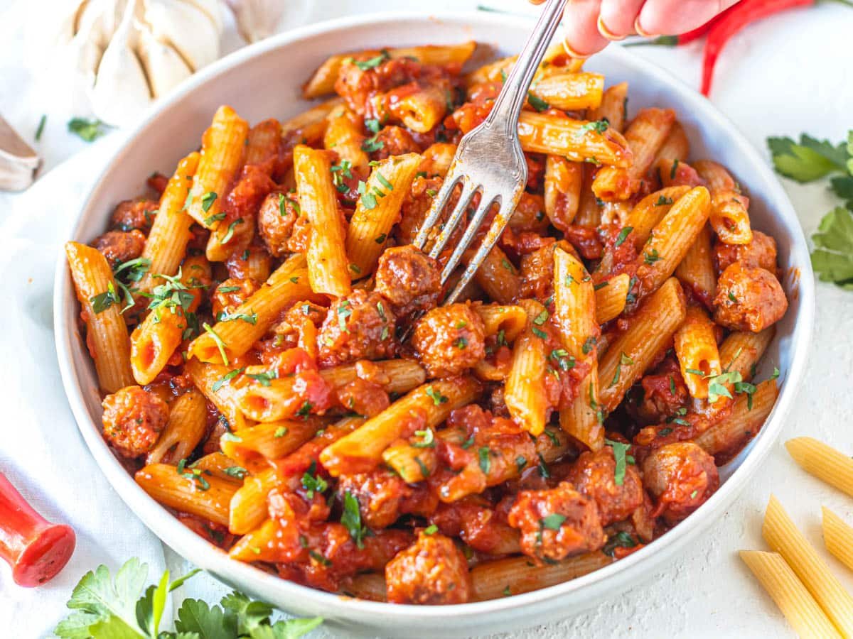 Penne Arrabbiata in a bowl with sausage and a silver fork
