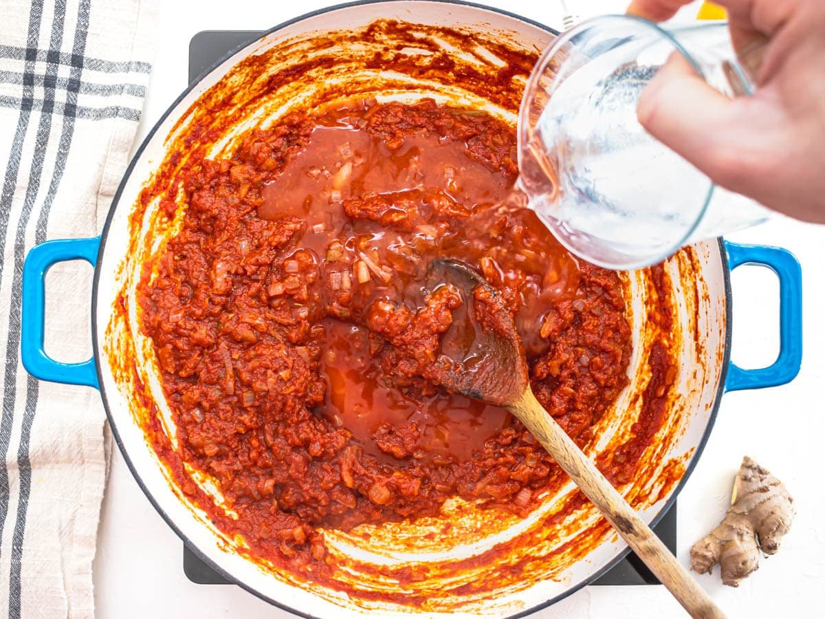 adding water to blue skillet with tomato sauce