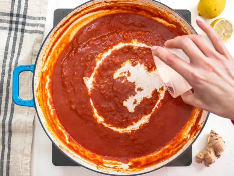 Hand adding cream to a skillet with tomato sauce