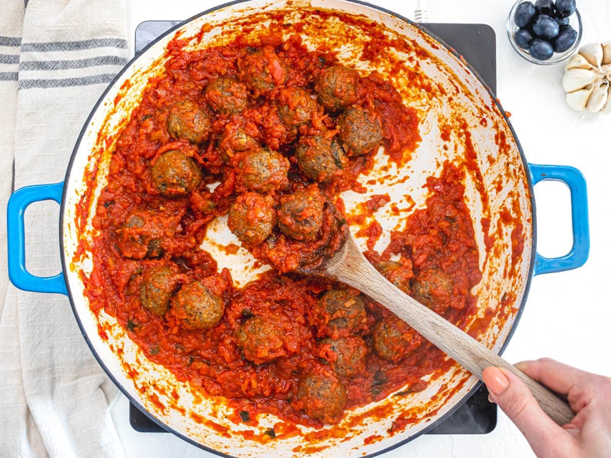 Vegan meatballs in a rich marinara sauce and a wooden spoon