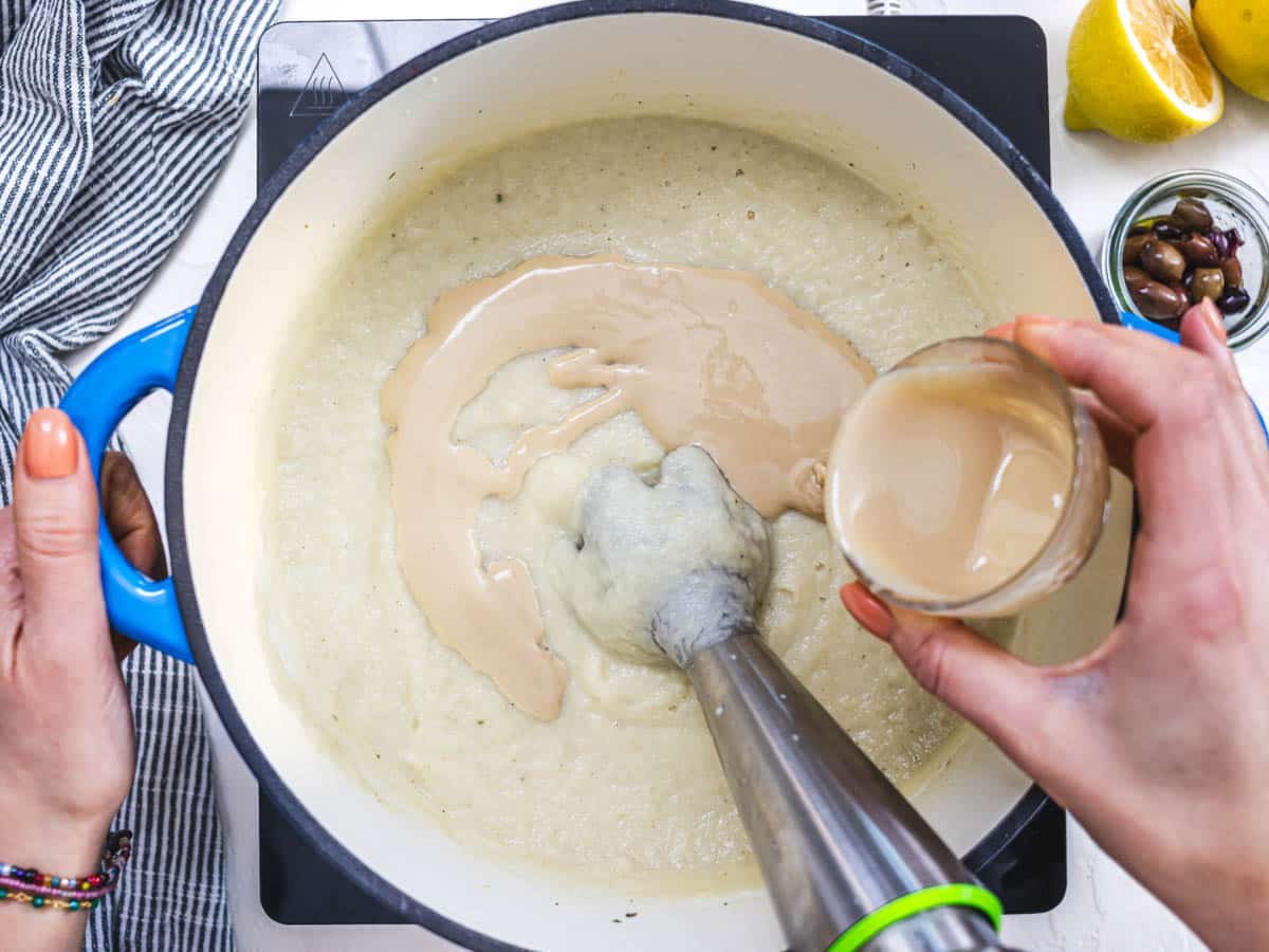 hand drizzling tahini into a casserole with cauliflower soup