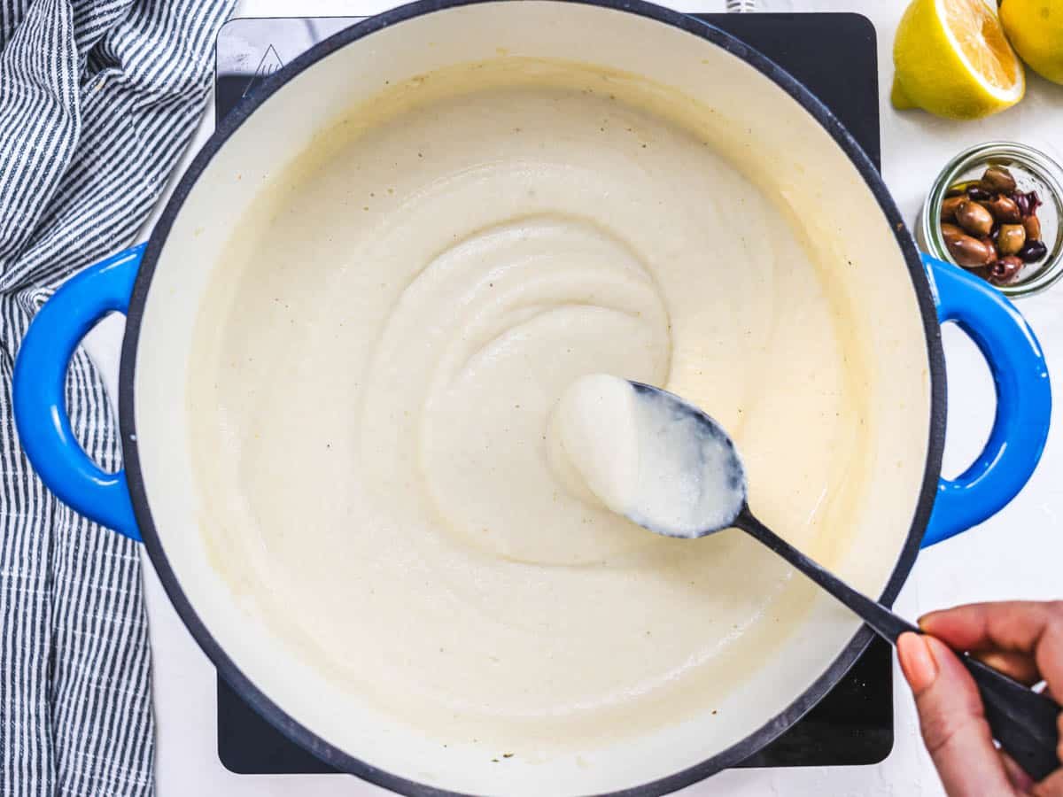 creamy cauliflower soup with a hand holding a black spoon