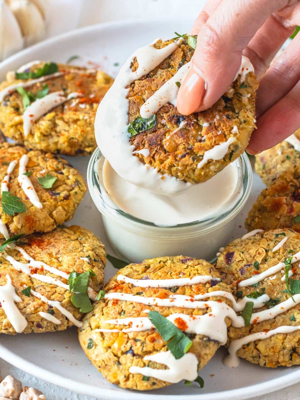 chickpea fritters dipped in creamy tahini sauce with a hand