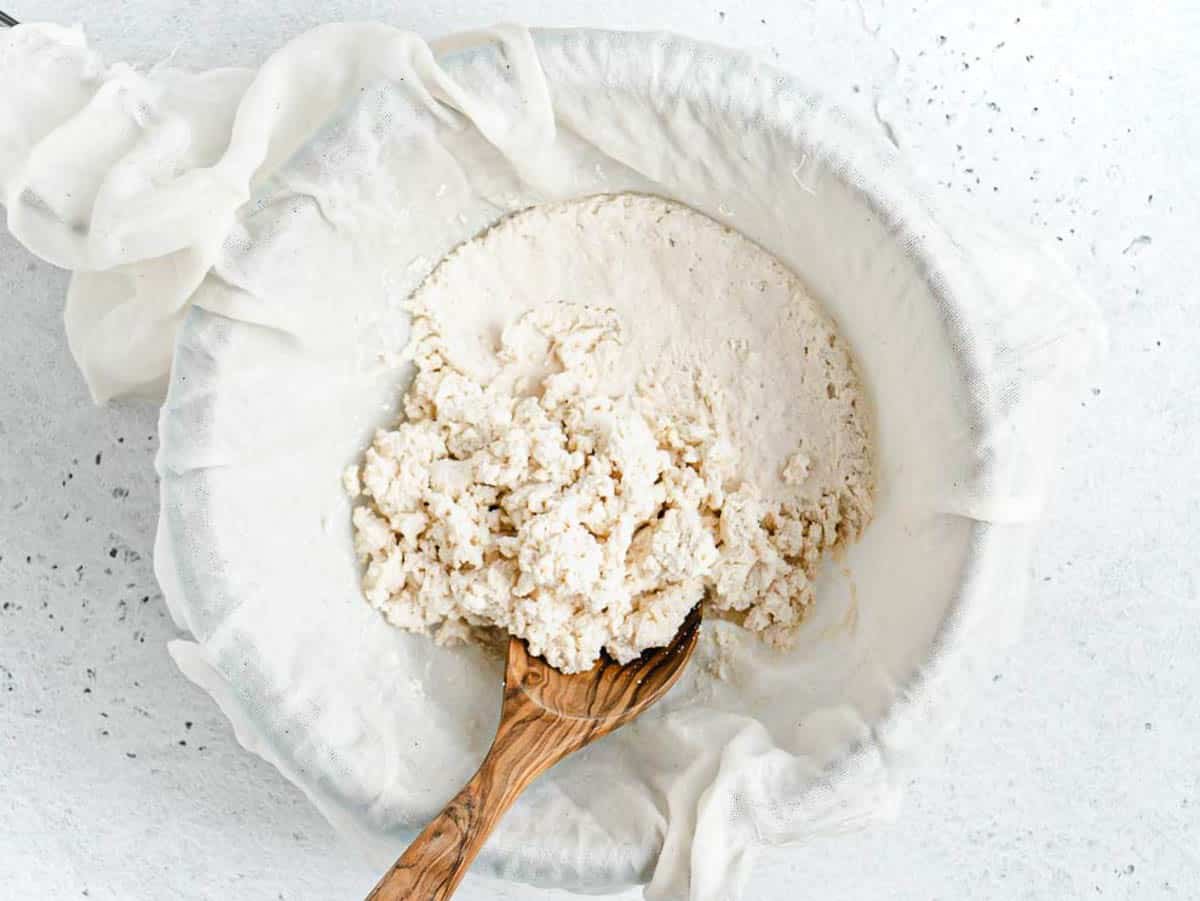 dairy-free ricotta in a sift with a wooden spoon