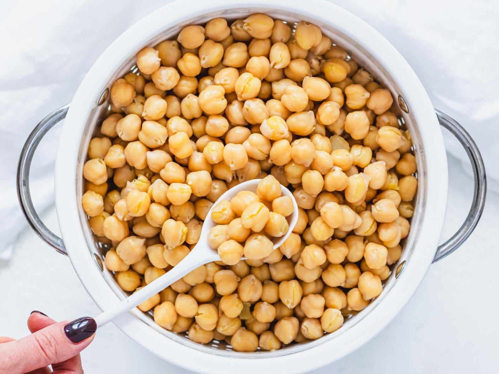 cooked tender chickpeas in a white sift with hand holding a white spoon