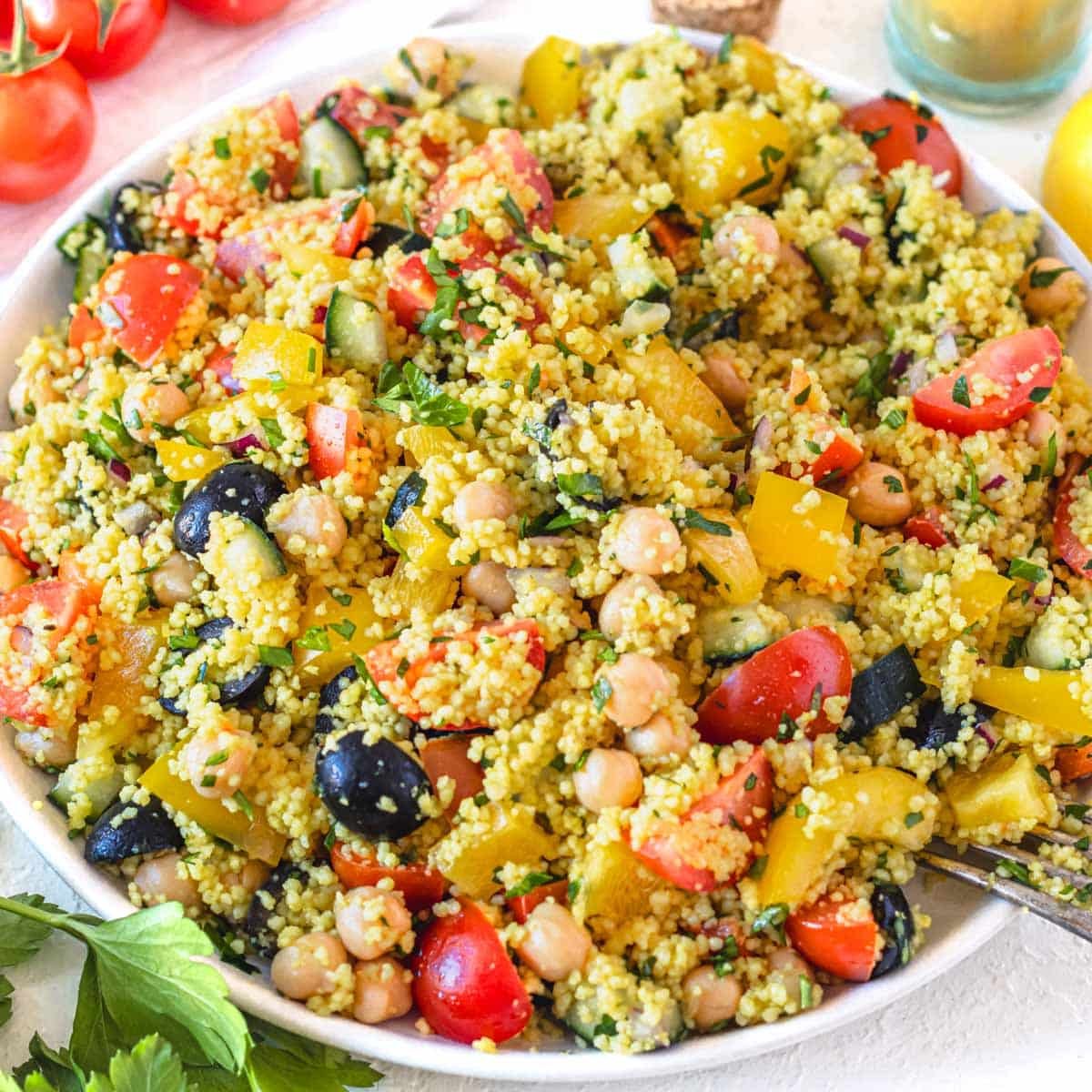 Chickpea couscous salad on a white plate with olives and bell pepper