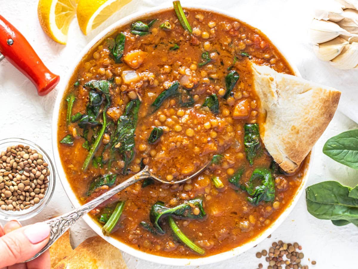 Easy lentil vegetable soup with pita bread and hand holding a silver spoon