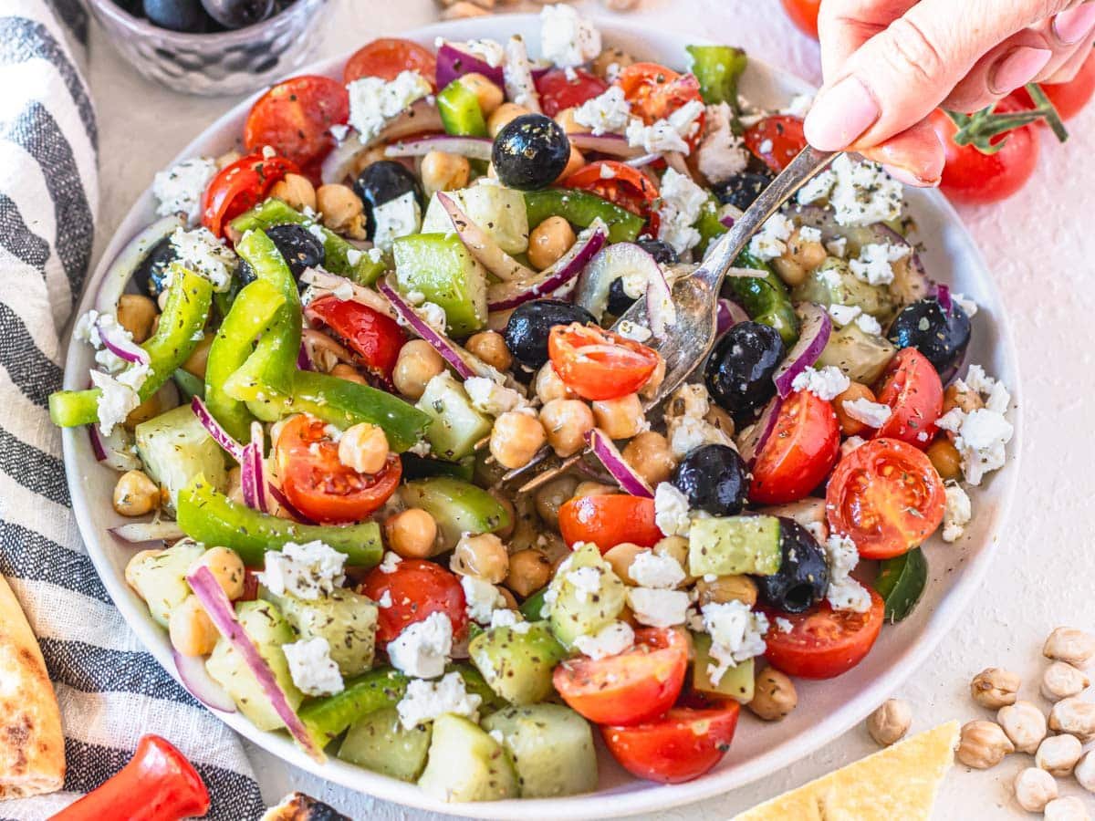 Greek chickpea salad with hand holding a silver fork