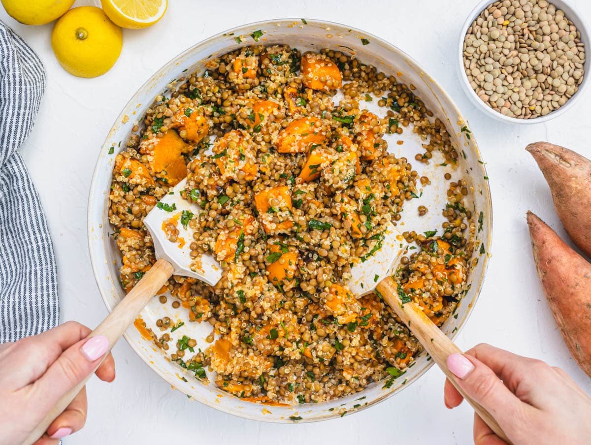 Hands mixing lentil and quinoa salad in a white bowl