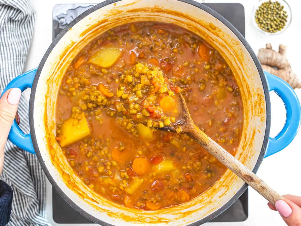 Mung beans and potatoes in a soup with hand holding a wooden spoon