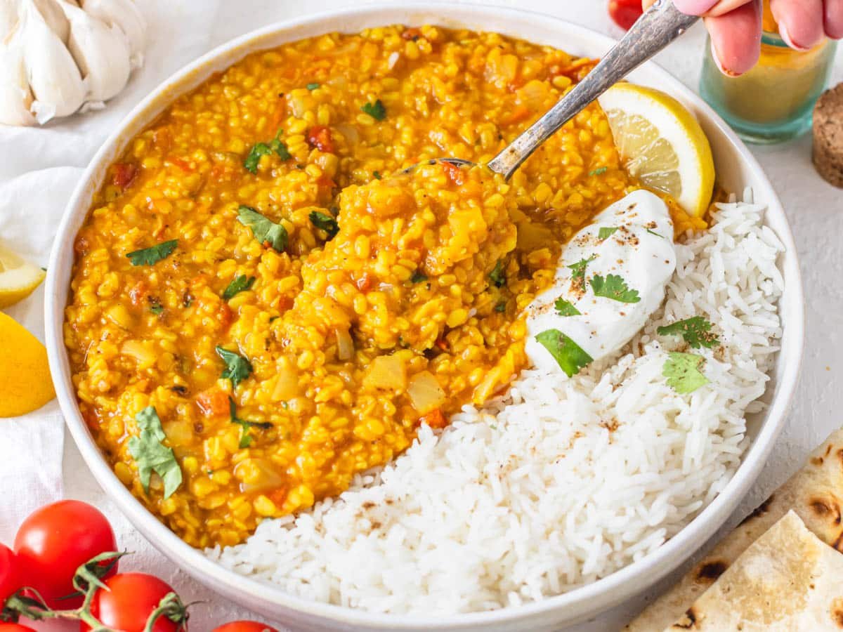 Mung dal with split mung beans and basmati rice with hand holding a silver spoon